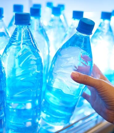 Human hand taking mineral water from shelf in supermarket